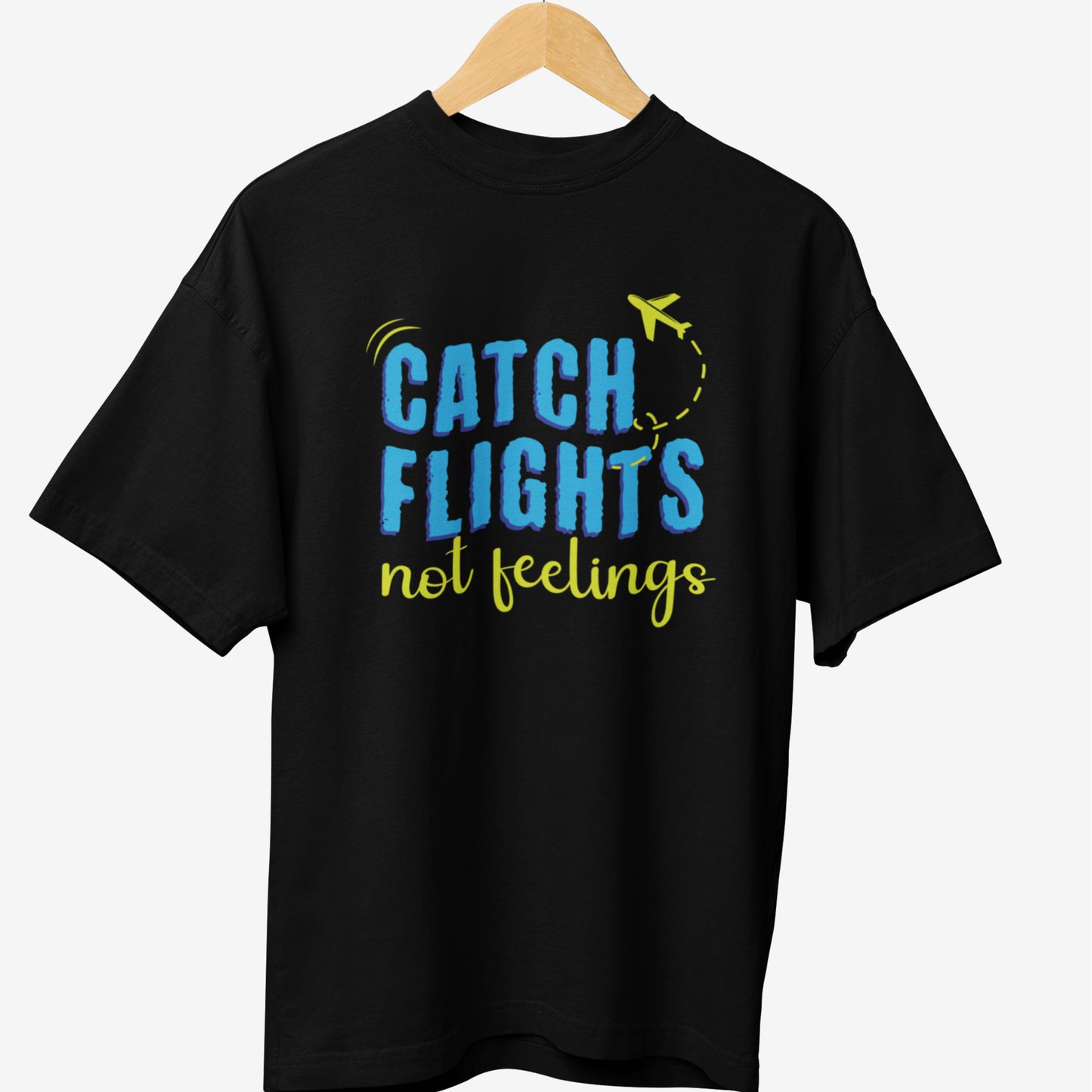 Black travel t-shirt featuring a vibrant typographic design with the phrase 'CATCH FLIGHTS not feelings' in blue and yellow, along with a small airplane graphic and a dotted flight path.
