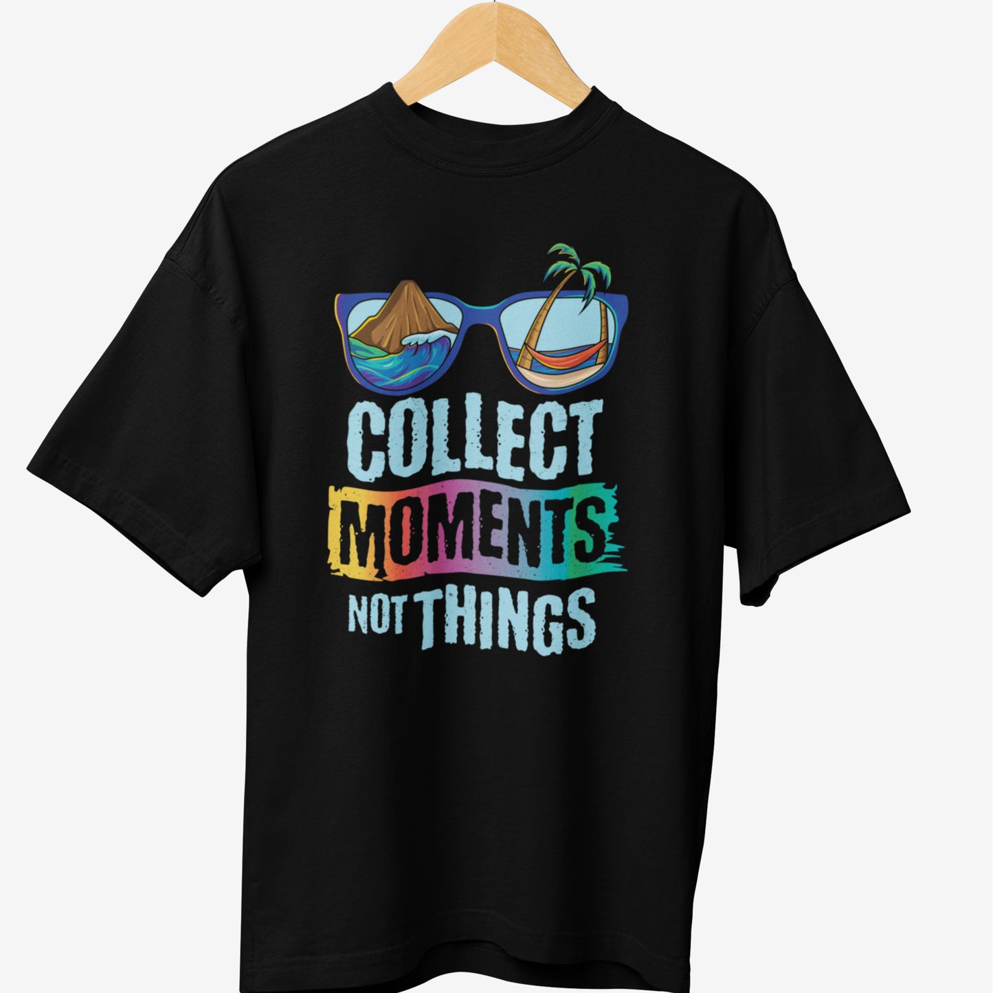 Black travel t-shirt featuring a colorful design with the phrase 'COLLECT MOMENTS NOT THINGS' in bold typography, along with sunglasses reflecting tropical beach and mountain scenery.